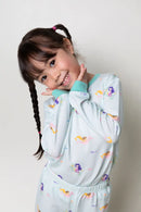 Young girl wearing a light turquoise pajama set with colorful mermaid patterns and small fish swimming