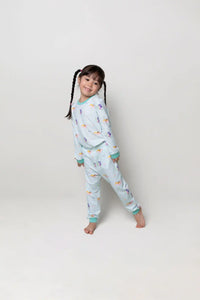 Child wearing a light turquoise pajama set with colourful mermaid prints on a white background and smiling.